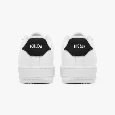 A pair of white low-top sneakers shown from the back, featuring a black heel tab with white text reading 'FOLLOW' on the left shoe and 'THE SUN' on the right shoe, set against a plain light gray background.