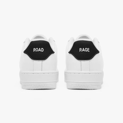 Rear view of white low-top sneakers showing contrasting black heel tabs labeled "ROAD" and "RAGE" above flat white rubber soles.