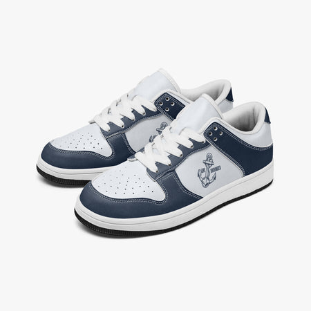 Angled three-quarter view of low-top sneakers in navy blue and white leather, featuring an anchor graphic with "STAY GROUNDED", white laces, and white inner lining.