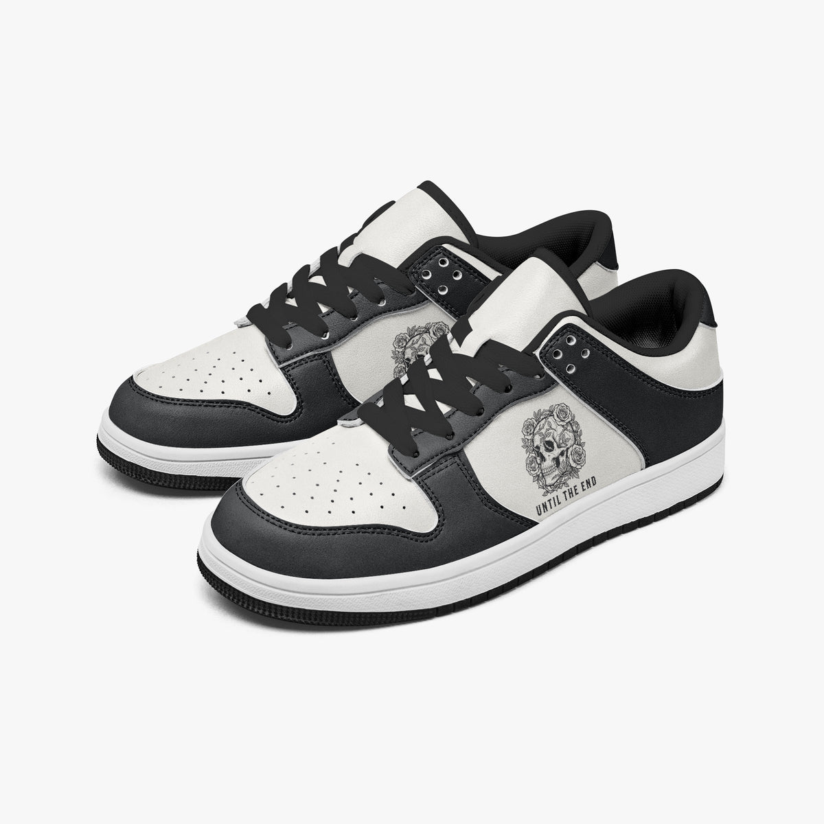 Angled three-quarter view of low-top sneakers in charcoal black and white leather, featuring a floral skull graphic with "UNTIL THE END", black laces, and a black inner lining.