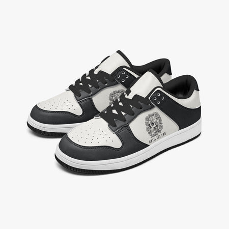 Angled three-quarter view of low-top sneakers in charcoal black and white leather, featuring a floral skull graphic with "UNTIL THE END", black laces, and a black inner lining.
