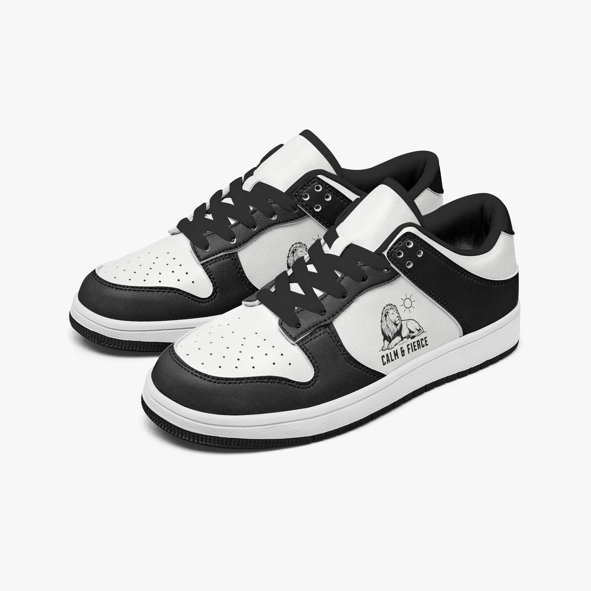 Angled three-quarter view of low-top sneakers in charcoal black and white leather, featuring a lion graphic with "CALM & FIERCE", black laces, and a black inner lining.