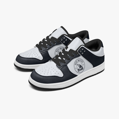 Angled three-quarter view of low-top sneakers in dark navy and white leather, featuring a breaching whale emblem with "DEEP WATERS", black laces, and a black inner lining.