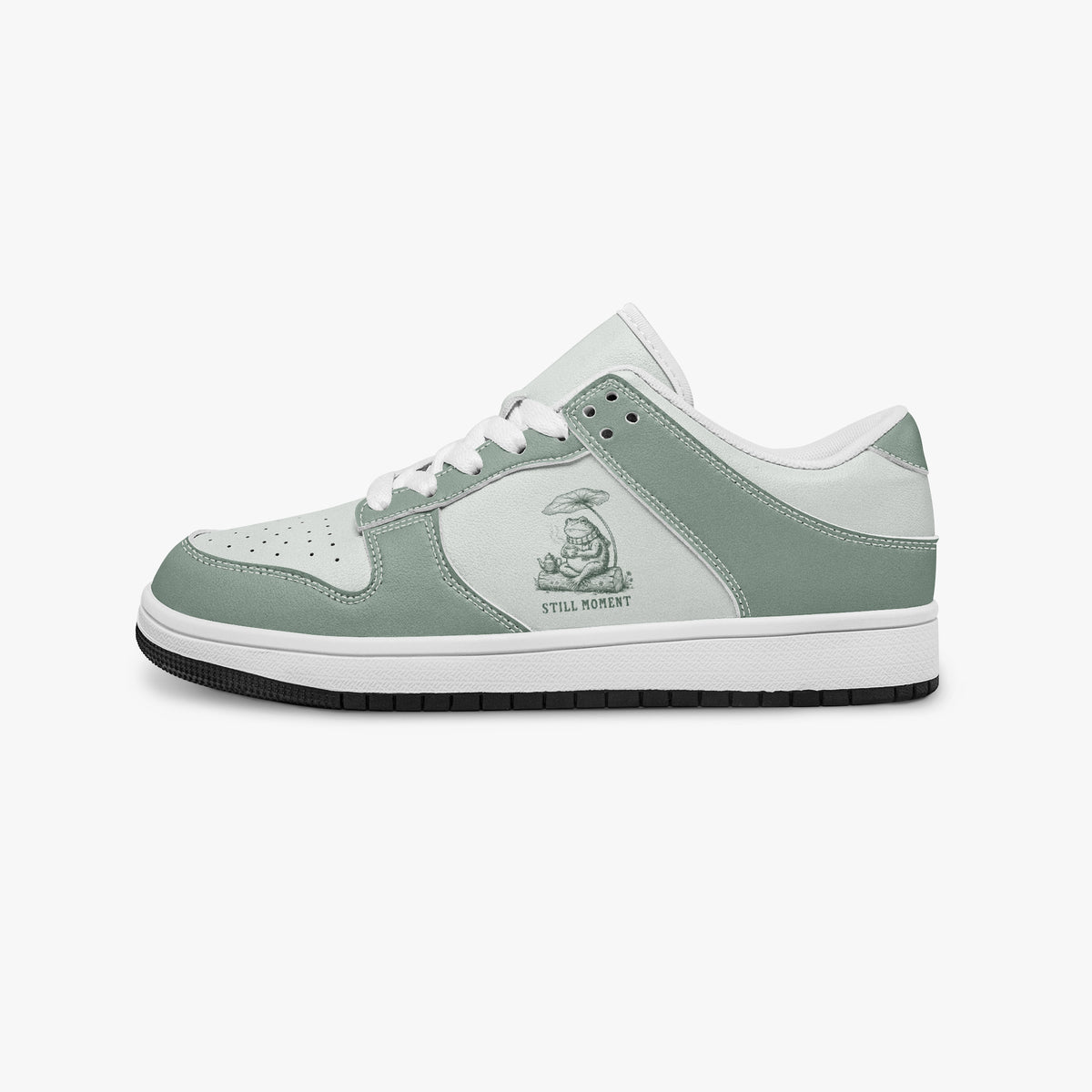 Side profile view of the left sneaker in sage green and off-white leather, highlighting the "STILL MOMENT" frog illustration, white laces, white interior lining, and flat rubber sole facing right.