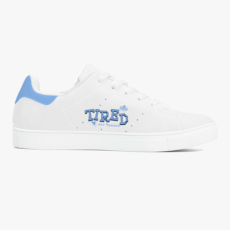 A white low-top sneaker with a light blue heel tab, white laces, and a blue 'TIRED' graphic on the side, shown against a plain white background.